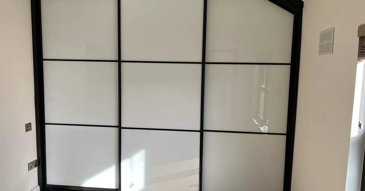 Angled installation of custom made sliding wardrobe doors featuring black framed sliding wardrobe doors and white glass panels, designed as premium custom sliding wardrobe doors for sliding wardrobe doors Ireland bedrooms.